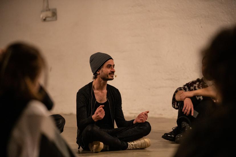 Raphaël Beau sitting on the floor and speaking to people.