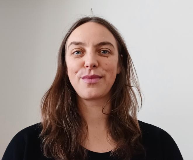 A headshot of Jana Unmüßig, whos wearing has a black shirt and has a long brown hair.