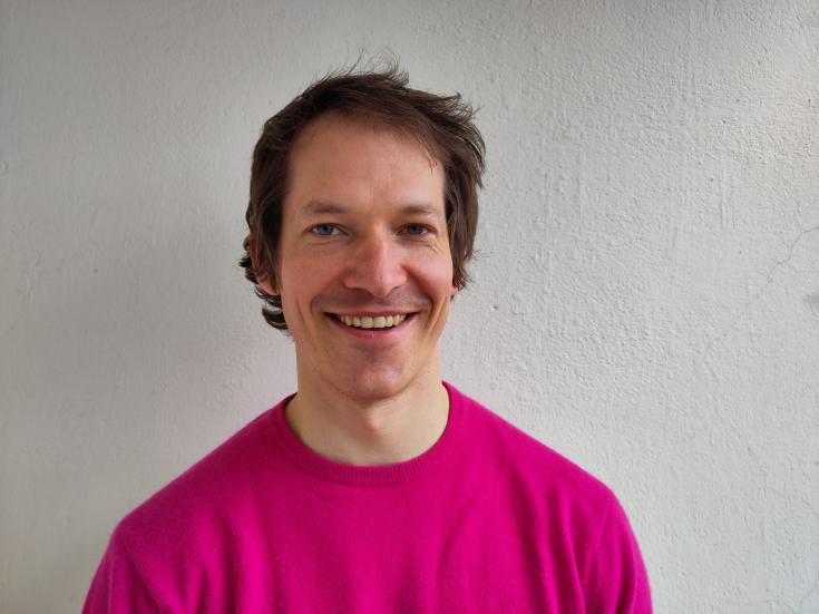 A head shot of smiling Elias Girod, he has a dark short hair and a pink shirt.