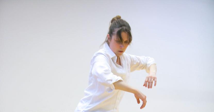 Liisa Risu in a white space, wearing a white collar shirt in an dancing position